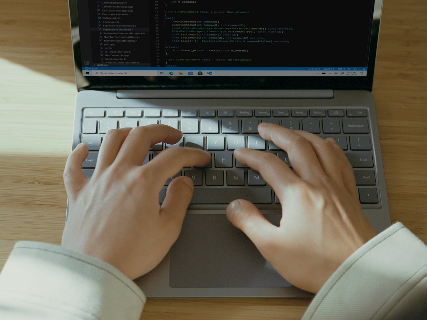 Person's hands typing code on a laptop keyboard at a wooden desk.